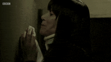 a woman praying in front of a wall with the bbc logo on the bottom