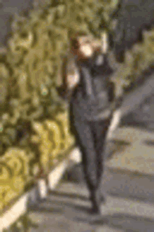 a blurry picture of a person walking down a sidewalk next to a fence .