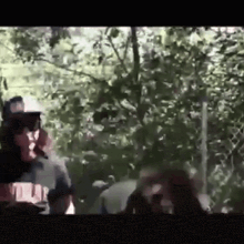 a man is smoking a cigarette in the woods while another man looks on .