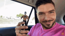 a man in a pink shirt is holding a toy figure of a man with a tattoo on his chest
