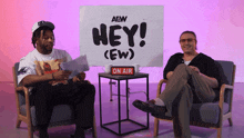 two men are sitting in front of a sign that says hey