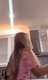 a woman in a pink shirt is standing in a kitchen with a light coming from the ceiling and the words tea4ruts visible