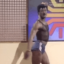 a man in a sheer top and shorts is dancing in front of a screen .