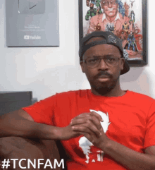 a man wearing glasses and a red shirt with the hashtag #tcnfam on the bottom
