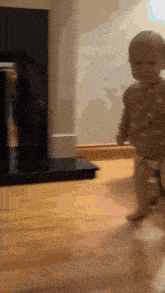 a baby is walking on a wooden floor in a room