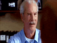 a man with gray hair and a mustache wearing a blue shirt is talking to someone