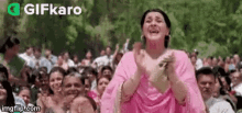 a woman in a pink dress is applauding in front of a crowd of people .