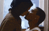 a man and woman kissing in front of a window .