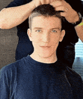 a man is getting his hair cut by another man while wearing a black shirt .