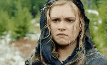 a woman wearing a scarf and a hood is looking at the camera with a serious look on her face .