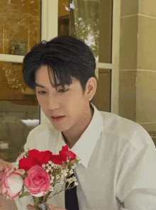 a man in a white shirt and tie is holding a bouquet of roses