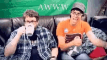 two men are sitting on a couch with a green background that says awwww