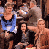 three women are sitting on a couch with a man in a suit standing behind them