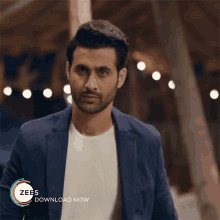 a man wearing a blue jacket and a white t-shirt is standing in front of a sign that says zees download now