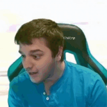 a man in a blue shirt is sitting in a green racer chair .
