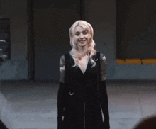a woman in a black dress and black gloves is standing in a parking garage .