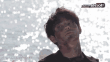 a man with a bandage on his face stands in front of a body of water with the word kamen rider on the bottom