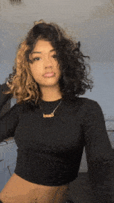 a woman with curly hair is wearing a black crop top and a gold necklace with the word love on it