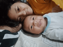 a woman and a baby are laying on a bed and the baby has a blue shirt on