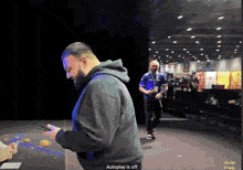 a man in a black hoodie is looking at his phone with the words " autoplay is off " on the bottom right