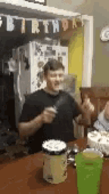 a man is sitting at a table with a green cup and a birthday banner behind him .