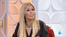 a woman with long blonde hair and a necklace is sitting in front of a microphone .