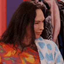 a woman with long hair is wearing a tie dye shirt and a towel around her neck
