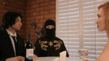 a man in a mask sits at a table with two other people