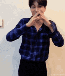a man wearing a blue plaid shirt covering his mouth with his hands