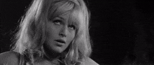 a black and white photo of a woman with blonde hair and bangs in a dark room .