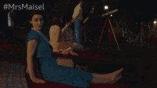 a woman in a blue dress sits on a red blanket with the hashtag #mrsmaiset