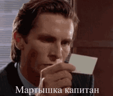 a man in a suit and tie is holding a card in his hand with the words " мартышка капитан " on it