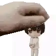 a hand is holding a small doll on top of a white surface .