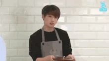a young man wearing an apron is standing in front of a brick wall holding a piece of chocolate .