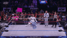 a woman in a blue dress holds a pink sign in a wrestling ring that says all elite