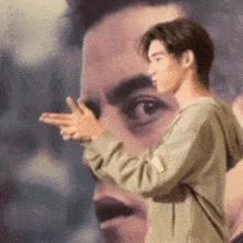 a man in a green sweatshirt is pointing at a painting of a man 's face .
