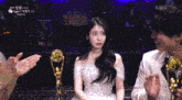 a woman in a white dress is sitting next to a man in a white suit and a trophy with kbs written on it