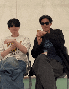 two men sitting next to each other one wearing a shirt that says " tokyo " on it