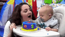 a woman and a baby are sitting in a high chair with a birthday cake .