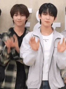 two young men are standing next to each other waving their hands .
