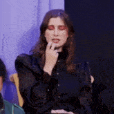 a woman in a black dress is sitting in a chair with her hand to her face .