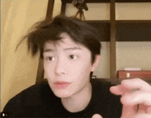 a young man with messy hair is making a funny face with his hand .