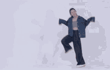 a woman in a denim jacket and wide leg pants is dancing on a white background