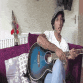 a man is sitting on a couch playing an acoustic guitar