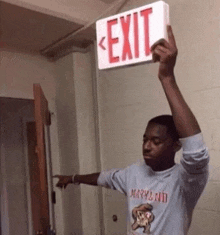 a man in a maryland shirt holds up an exit sign