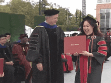 a woman in a graduation gown is holding a diploma