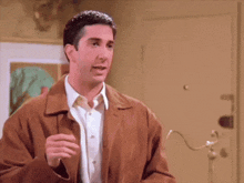 a man in a brown jacket is standing in front of a door
