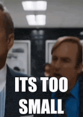 a man in a suit says it 's too small in front of another man in a blue shirt