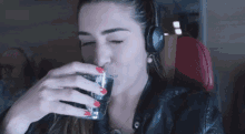 a woman wearing headphones is drinking from a glass while sitting on an airplane .