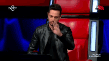 a man in a black leather jacket is sitting in a red chair with the words " karar senin " written on the screen